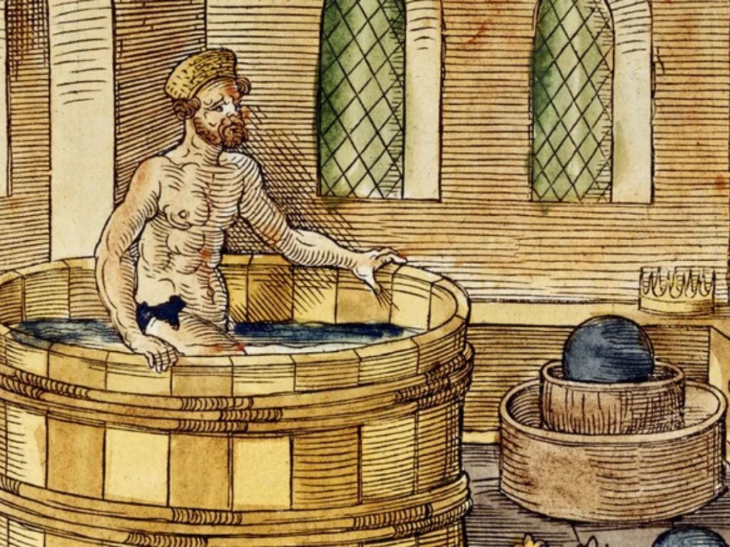 A naked man sits in a wooden barrel tub in a medieval bathhouse, reflecting how bathing was part of personal hygiene in the Middle Ages despite the lack of modern sanitation.