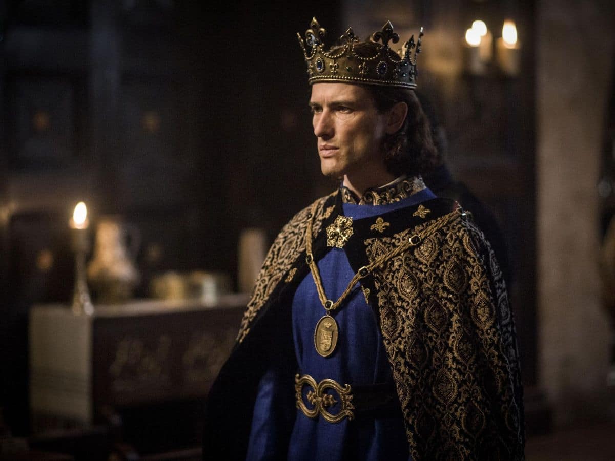 A dramatic scene of a man dressed as a medieval king in a richly embroidered robe and a golden crown, standing in a dimly lit royal hall. This cinematic portrayal reflects the regal legacy of the Capetians, emphasizing their cultural and political influence in medieval Europe.