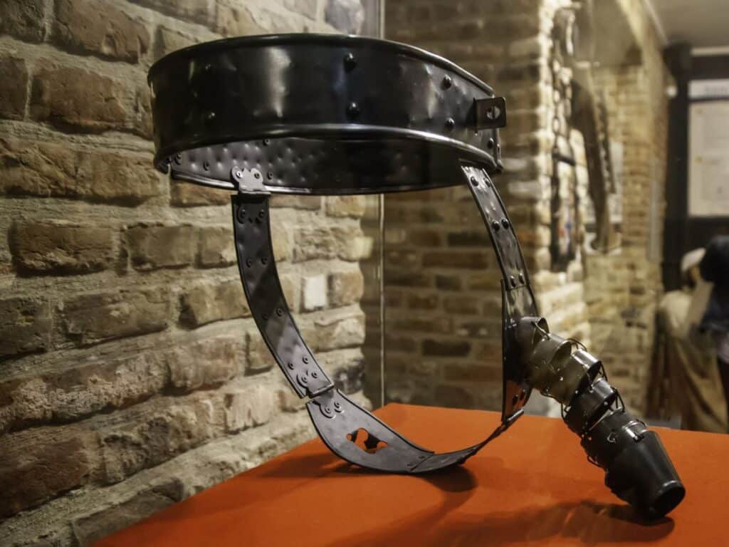 A modern museum display of a black metal chastity belt featuring heavy riveted construction, often used to question the historical accuracy of chastity belt use during the Middle Ages.