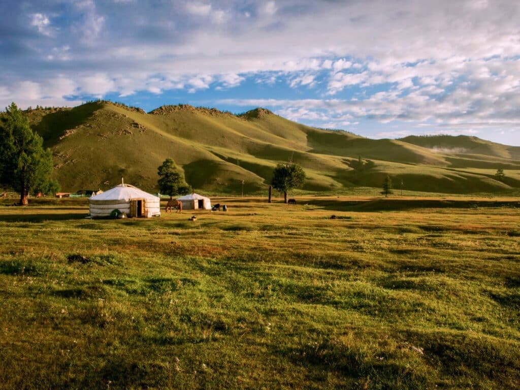 Traditional Mongolian yurts sit on the vast grassy steppe under a blue sky with rolling green hills in the distance—landscapes much like those traversed by Genghis Khan and his nomadic warriors. This serene view captures the heartland of the Mongol Empire’s origins.