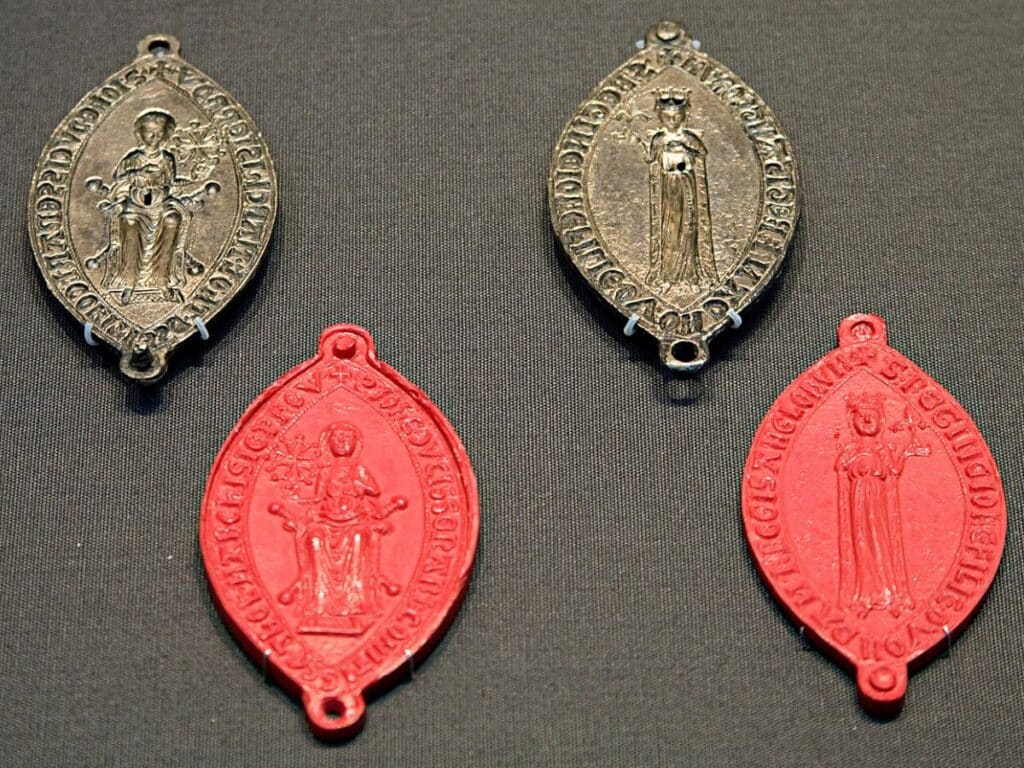 Display of four wax seals—two in red, two in black—bearing images of a crowned Joanna Plantagenet holding a fleur-de-lis, used for authenticating documents, showcasing her official role and authority as a royal woman of power.