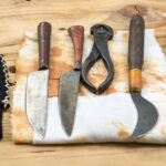 A set of medieval dental and surgical tools with wooden handles, including knives, pliers, and curved blades, laid out on a stained cloth, reflecting the primitive instruments used in dentistry in the Middle Ages.