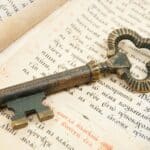 A close-up of an antique iron key lying on an open book with Cyrillic text, symbolizing the concept of unlocking secret knowledge or hidden messages during medieval times.