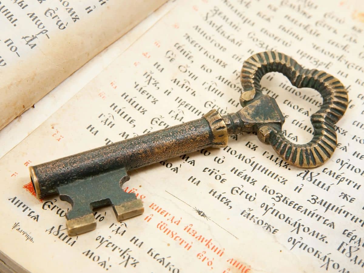 A close-up of an antique iron key lying on an open book with Cyrillic text, symbolizing the concept of unlocking secret knowledge or hidden messages during medieval times.