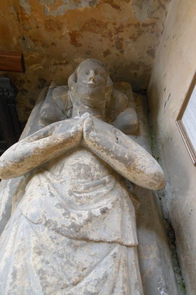 Stone effigy of a medieval woman lying with hands in prayer, possibly representing Ela of Salisbury, shown in weathered detail within a stone niche.
