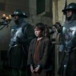 A dramatic color scene showing Lambert Simnel in ragged clothes flanked by armored guards in a royal court setting, depicting his capture after the failed rebellion and his fate under Henry VII.