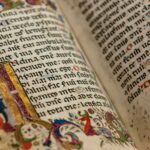 Close-up of a medieval illuminated manuscript with ornate gold and colored illustrations, showing Latin text in black ink with decorative initials and red rubrication, symbolizing the era when many now-common medieval sayings originated in religious and literary works.