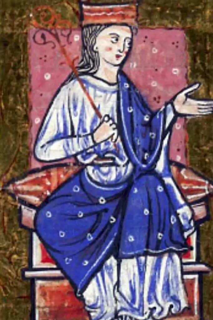 Medieval illustration of Æthelflæd, Lady of the Mercians, depicted seated on a throne wearing a blue robe and crown, holding a scepter and gesturing with one hand against a patterned backdrop.