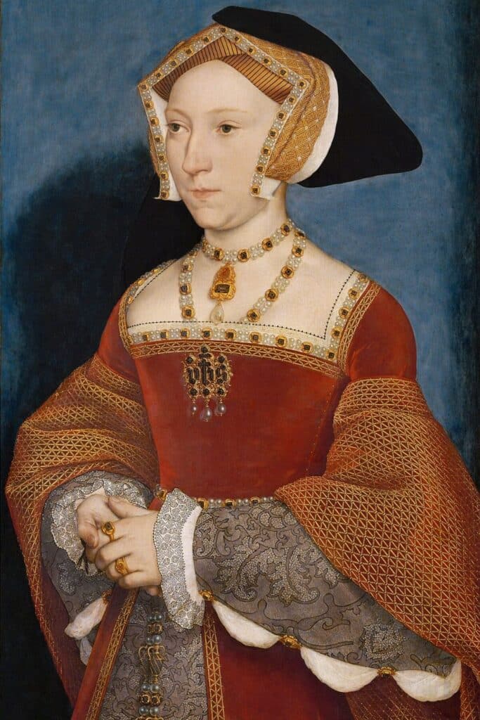 A formal Tudor portrait of Jane Seymour in a red gown adorned with gold embroidery and pearls, her hands gently clasped, highlighting Jane Seymour’s royal poise and refined beauty as queen consort.
