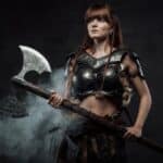A female Viking warrior dressed in fur and metal armor holds an ornate double-headed axe, standing confidently against a smoky, dark background.