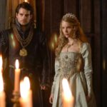 Scene from 'The Tudors' showing Catherine Howard and King Henry VIII in elaborate Tudor attire, standing solemnly in a dimly lit royal chamber with candlelight in the foreground.