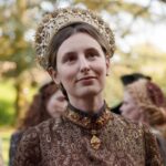 A modern actress portraying Margaret Pole in historical costume with an ornate gold crown and richly patterned dress, likely from a period drama or documentary recreation.