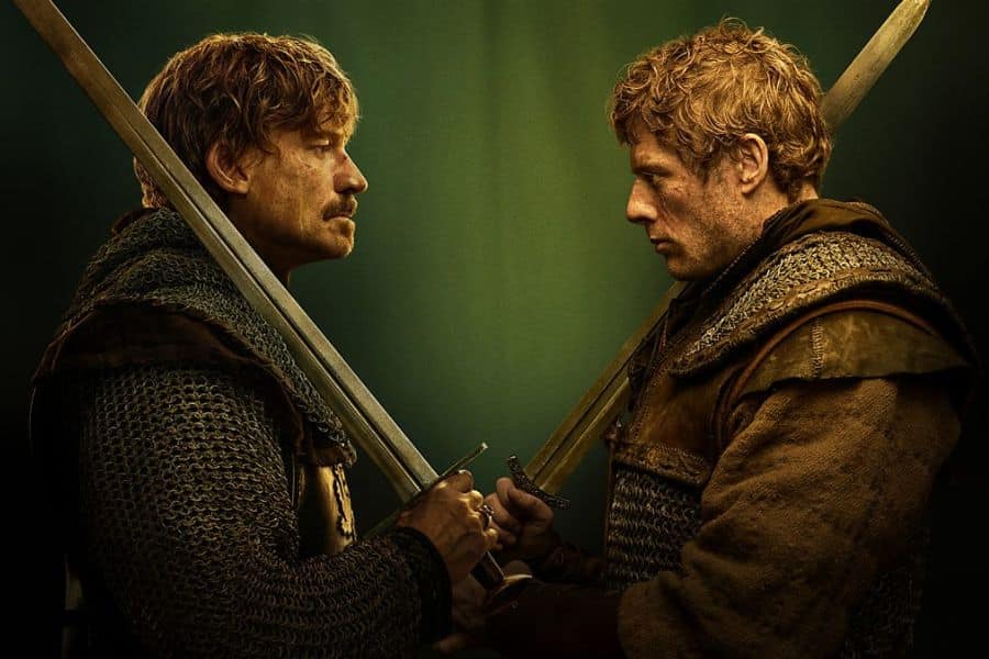 Two armored men stand face-to-face in intense confrontation with swords crossed in front of them against a moody green background. Promotional imagery from BBC One’s new historical drama, King & Conqueror.