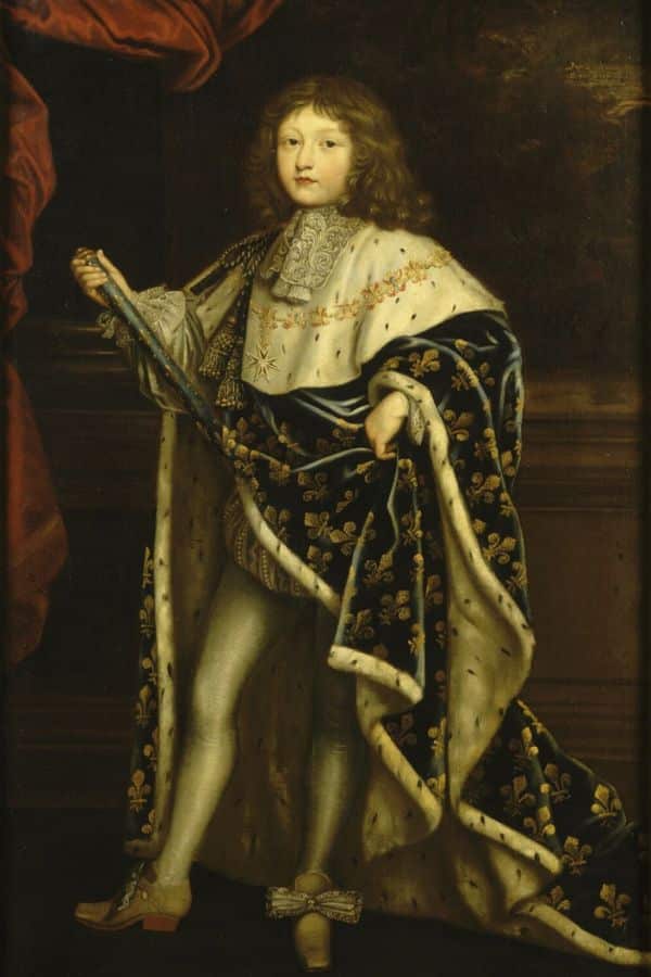 Louis XIV in royal attire, draped in a blue cloak with golden fleur-de-lis, holding a scepter and standing before heavy red curtains.