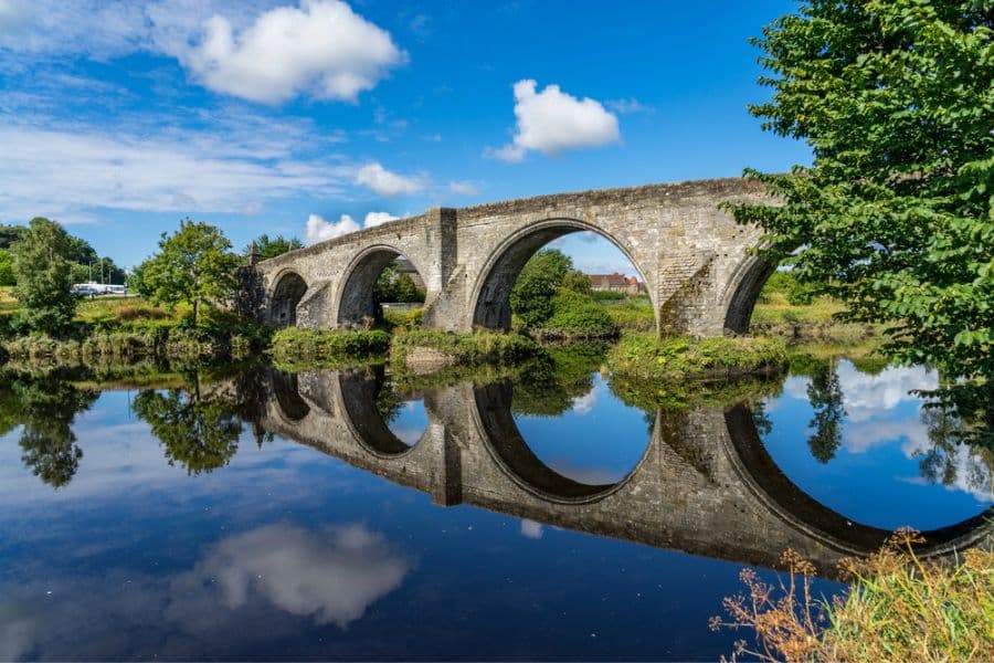 The medieval Stirling Bridge arches over a calm river, its stonework beautifully reflected in the water, representing a landmark tied to Stirling Castle’s history.