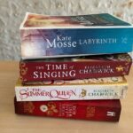 A stack of four historical novels set in the Middle Ages on a wooden table, including "Labyrinth" by Kate Mosse, two novels by Elizabeth Chadwick—"The Time of Singing" and "The Summer Queen"—and "The Last White Rose" by Alison Weir.