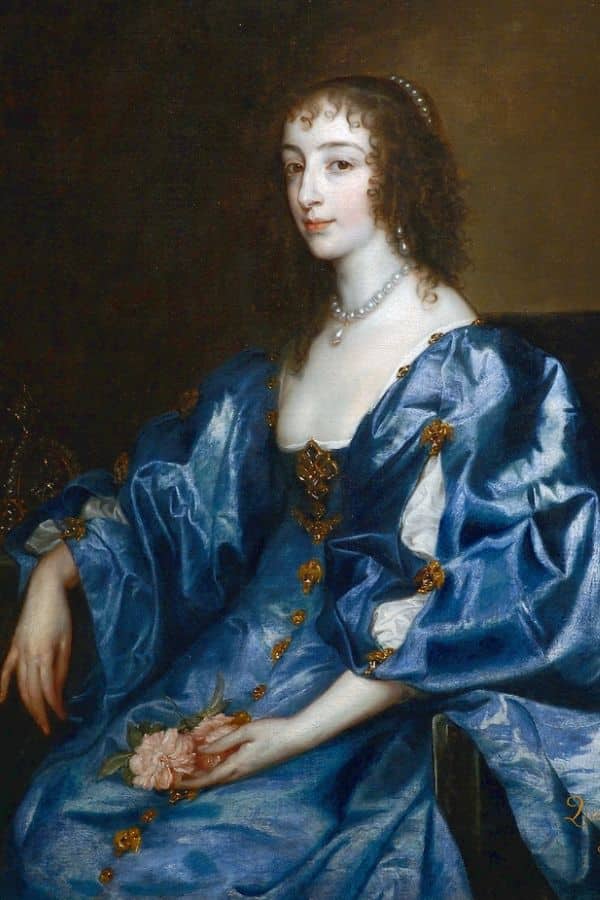 Elegant portrait of a noblewoman seated in a blue gown holding a pink rose, possibly Henrietta Maria or another court figure associated with George Villiers. Her calm demeanor and rich costume reflect the opulence of the era.