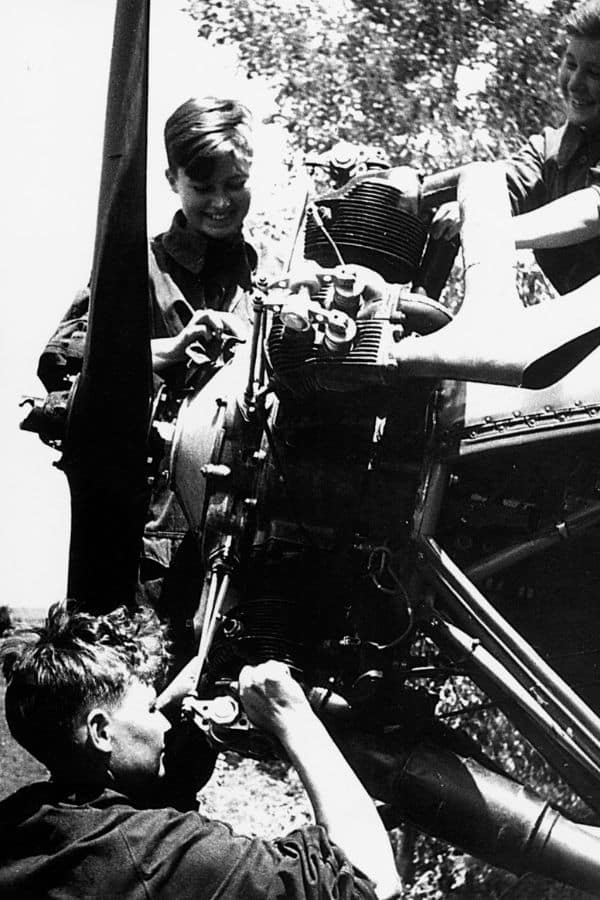 Two young women work on an aircraft engine alongside a male mechanic. These women were ground crew for the Night Witches, playing a vital role in keeping the planes mission-ready during WWII.