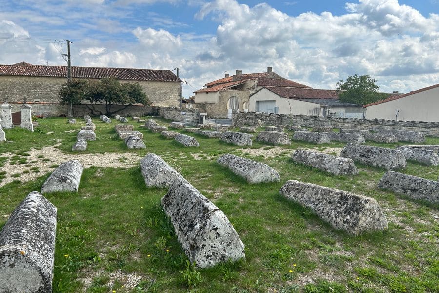 A wide shot of an ancient cemetery filled with rows of stone sarcophagi with pitched tops, set in grassy ground under a partly cloudy sky. The graves appear medieval, possibly linked to the Knights Templar.
