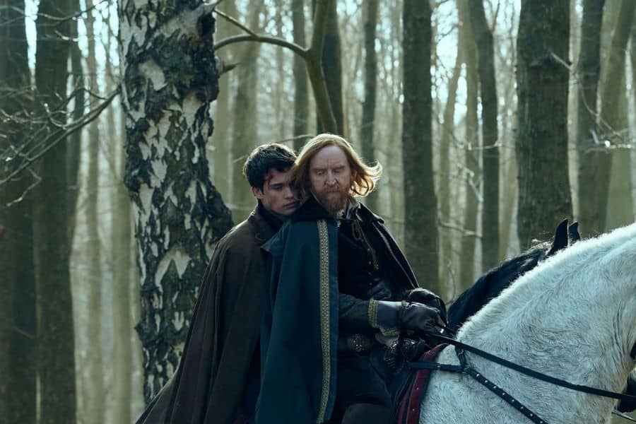 Cinematic still showing two men on horseback in a wintry forest, with one resembling a red-haired figure often portrayed as George Villiers in modern dramatizations. The emotional scene suggests a moment of tension or alliance.