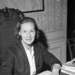 Marie-Madeleine Fourcade seated at a desk in a formal setting, shown mid-career as the head of France’s largest spy network during World War II.