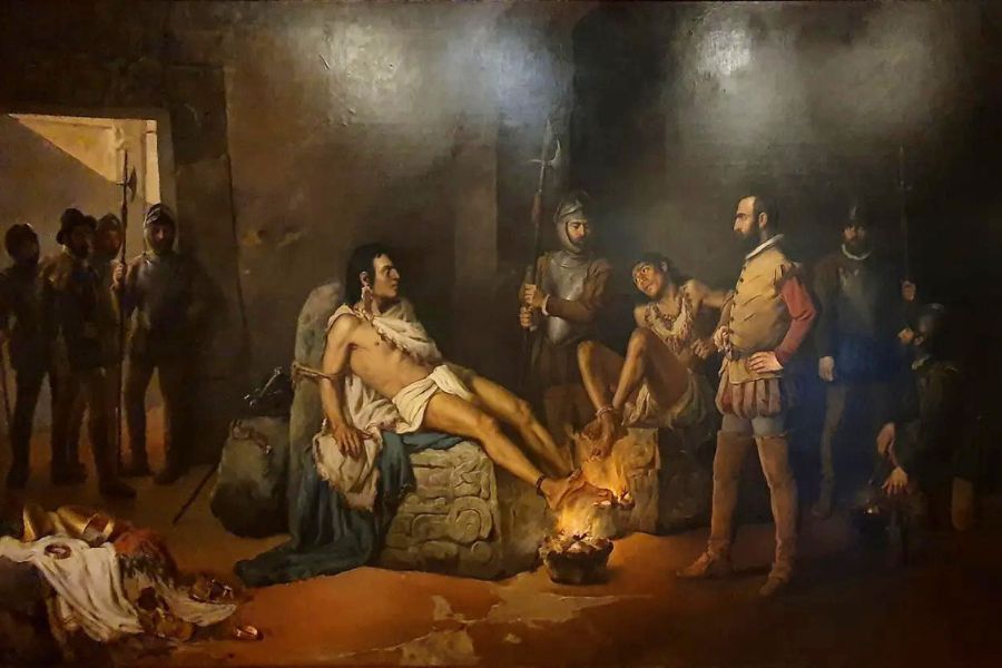 A captive ruler sits partly undressed beside a small fire in a dark stone chamber. Armed guards and officials surround him during an interrogation or imprisonment scene.