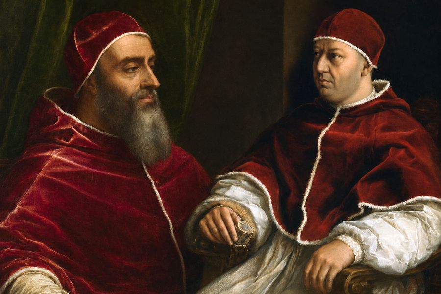 Two popes in red velvet robes sit together against a dark background. The older bearded figure faces forward while the younger man turns toward him in quiet conversation.