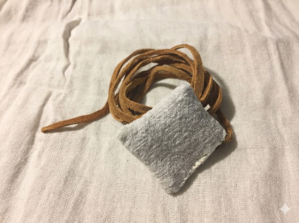 Reproduction of an early sheath style condom made from animal intestine and tied with a leather cord resting on white fabric. This artifact illustrates a historical barrier method often referenced in discussions of medieval contraception and premodern sexual health practices.