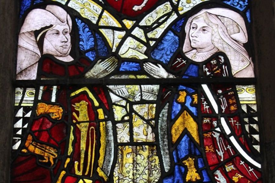 Medieval stained glass window depicting two noble figures facing one another beneath heraldic symbols and coats of arms. The artwork highlights the dynastic rivalries and family alliances that shaped the Wars of the Roses.