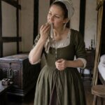 A woman in tudor dress cleaning her teeth with a rag