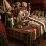 A bishop in ceremonial robes raises a blessing over a crowned couple lying together in an ornate bed while nobles crowd the room. The scene represents medieval wedding night customs in which clergy and court witnesses gathered around the marriage bed.