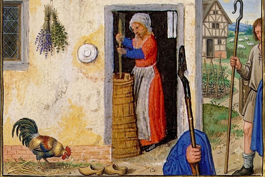 Medieval rural scene with a peasant woman churning butter in a doorway while a rooster pecks nearby and shepherds stand outside. Bundles of herbs hang from the wall beside the house.