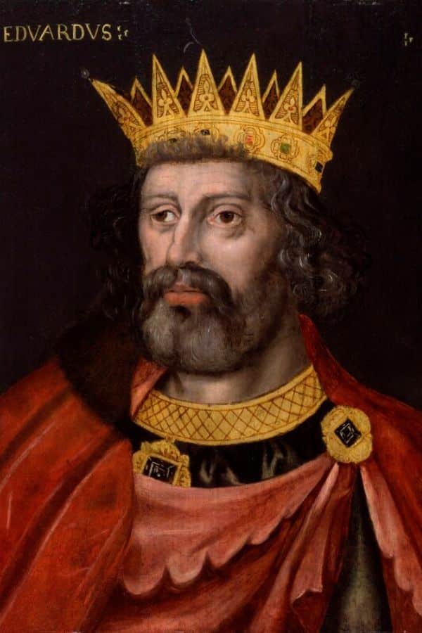 A crowned and bearded medieval monarch wears a red cloak over richly decorated clothing against a dark background. The inscription "EDVARDVS" appears in the upper left corner.