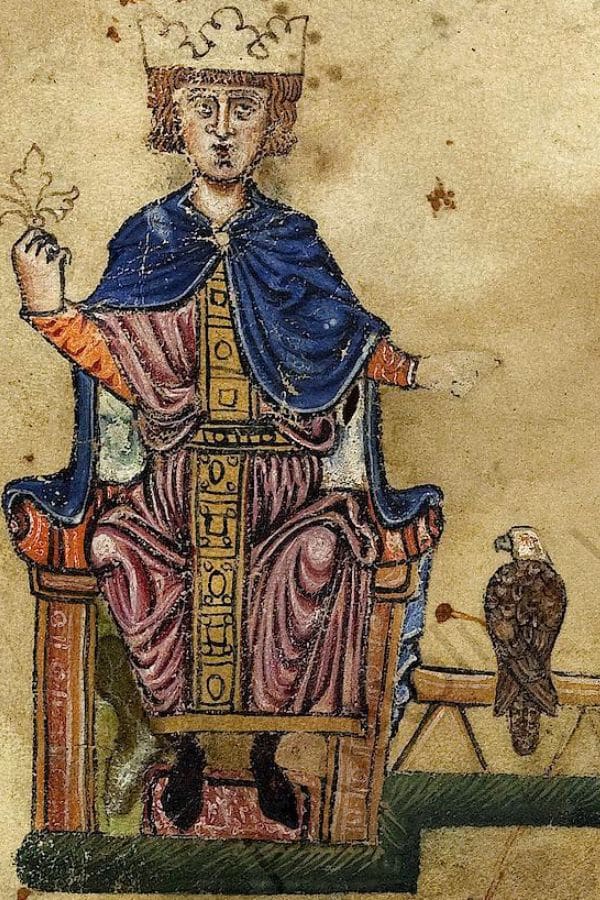 A crowned ruler sits on a wooden throne in a medieval manuscript illustration while holding a fleur de lis. A tethered falcon rests on a nearby perch as a symbol of royal status and courtly life.
