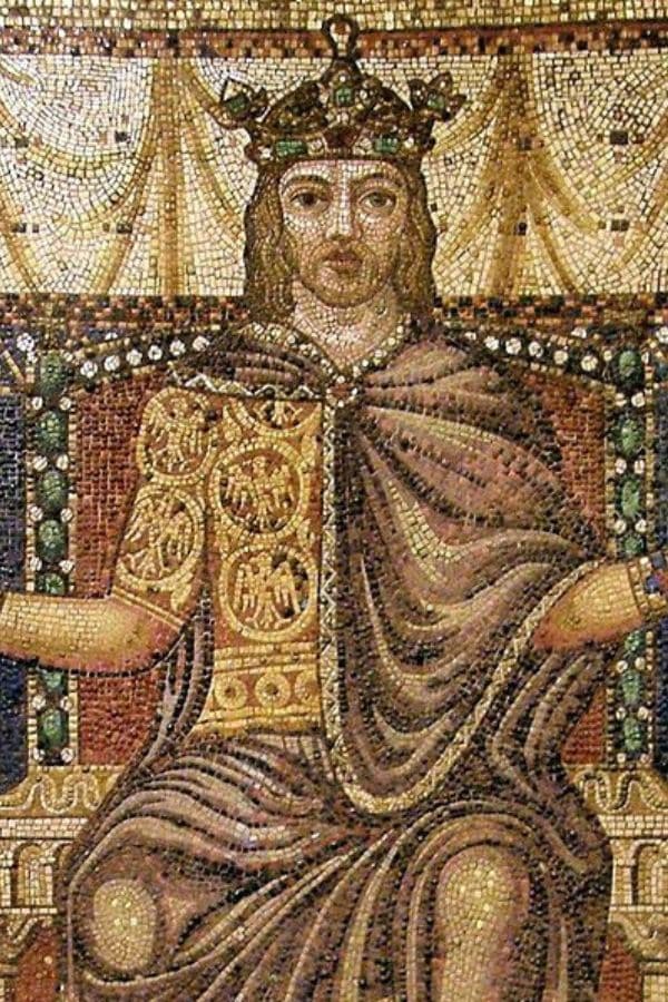 A mosaic shows a crowned medieval monarch seated on an elaborate throne beneath draped fabric. His jeweled crown and richly patterned robes convey the wealth and ceremony of kingship.