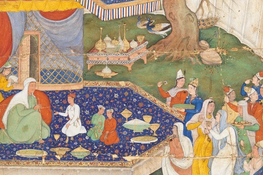 A historical miniature depicts women and attendants gathered for a feast beside a tent and large tree. Colorful robes dishes and serving vessels fill the scene with an elaborate blue floral carpet covering much of the ground.