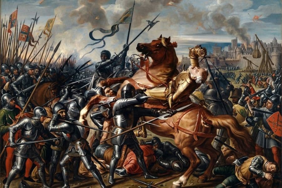 Medieval knights clash on horseback and on foot in a crowded battlefield filled with lances banners and armored soldiers. A knight in gold armor falls backward from his horse as fighting surrounds him and smoke rises near a fortified city.
