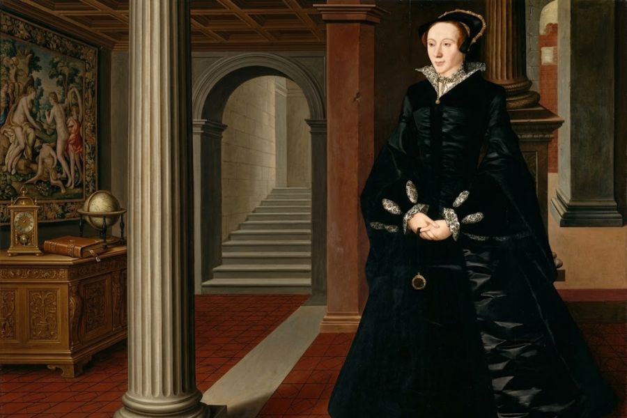 Full length painted portrait of a Tudor era woman dressed in an elaborate black gown with white lace at the collar and cuffs. She stands inside a grand columned room beside a cabinet holding books a clock and a globe.