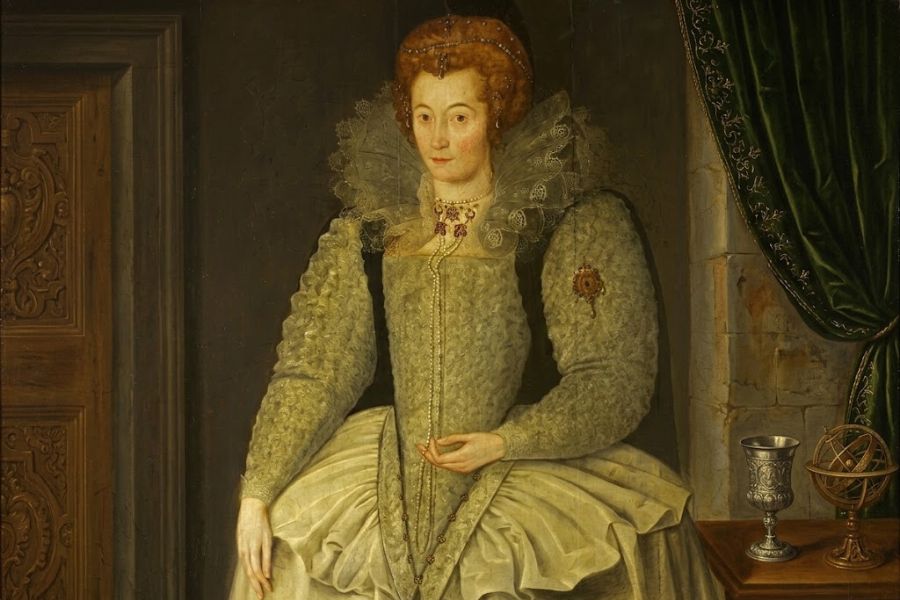 Painted portrait of a Tudor era woman in a pale green embroidered gown with an enormous ruff and structured skirt. A silver cup and an astronomical instrument sit beside her in the richly furnished interior.