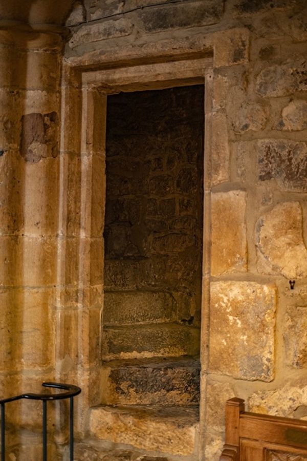 Curving stone staircase behind a pointed arch doorway inside a medieval church. The narrow stairway appears to lead upward toward the rood loft.