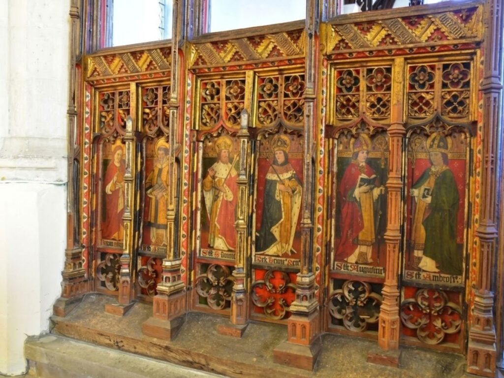 Ornately painted Gothic wooden panels decorated with religious figures in red gold and green. The carved screen forms part of the decorative structure associated with the rood loft.