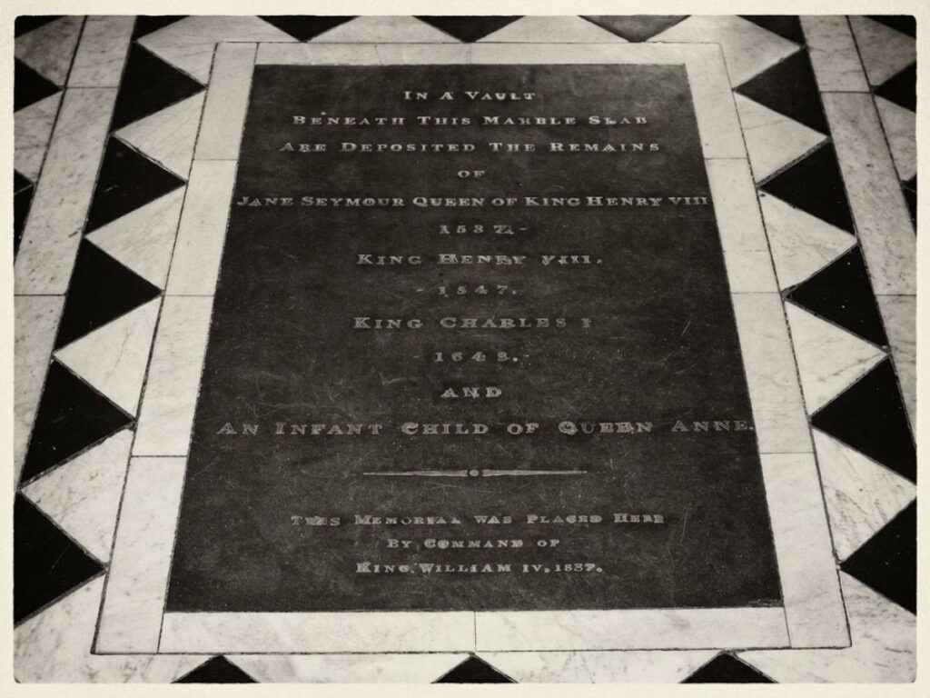 A black and white photograph of the marble burial marker for Henry VIII and other royals in St Georges Chapel. The inscription reads "In a vault beneath this marble stone are deposited the remains of Jane Seymour Queen of King Henry VIII 1537. King Henry VIII 1547. King Charles I 1648. And an infant child of Queen Anne. This memorial was placed here by command of King William IV 1837."