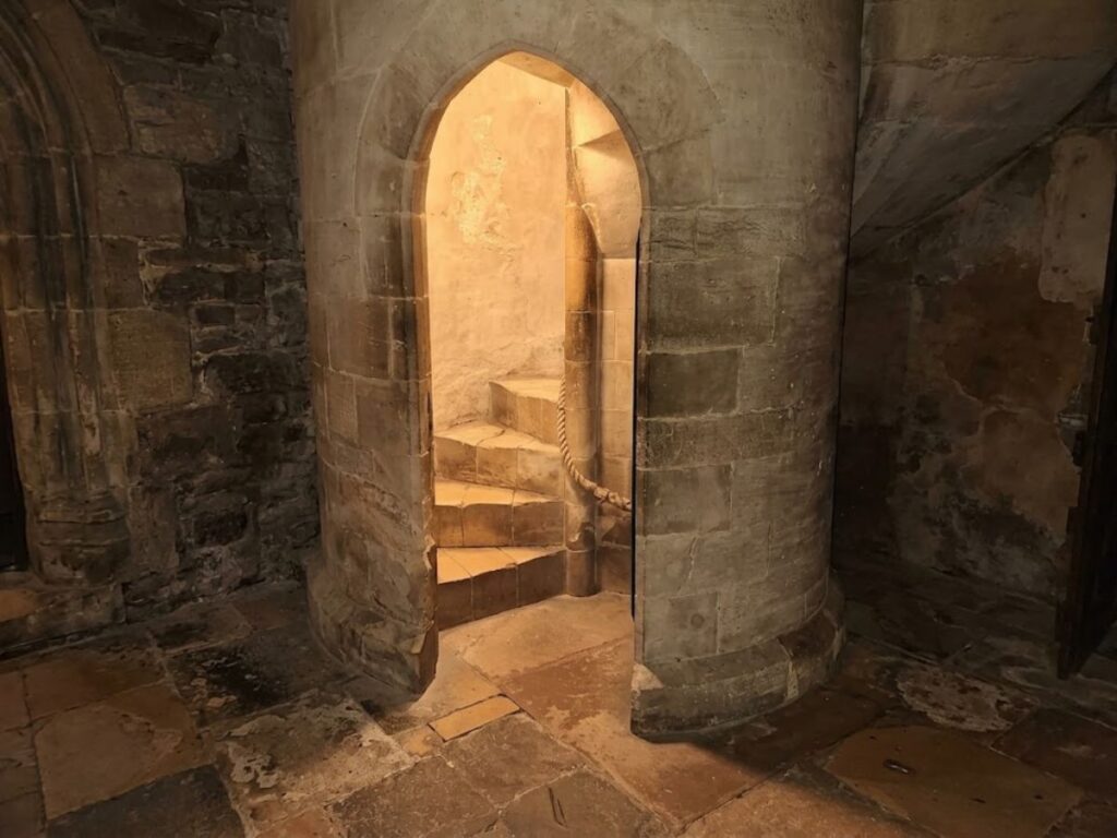 Curving stone staircase behind a pointed arch doorway inside a medieval church. The narrow stairway appears to lead upward toward the rood loft.